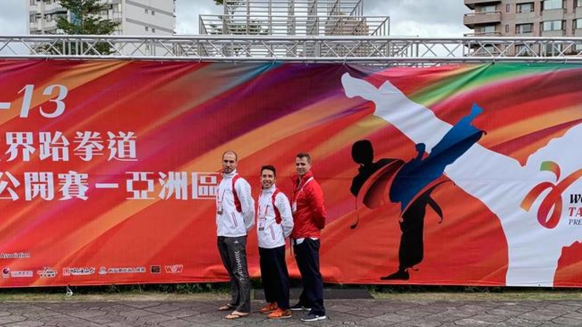 Els tres integrants de la selecció espanyola de taekwondo posen al costat d’un dels cartells que anuncien el Mundial a Taipei.