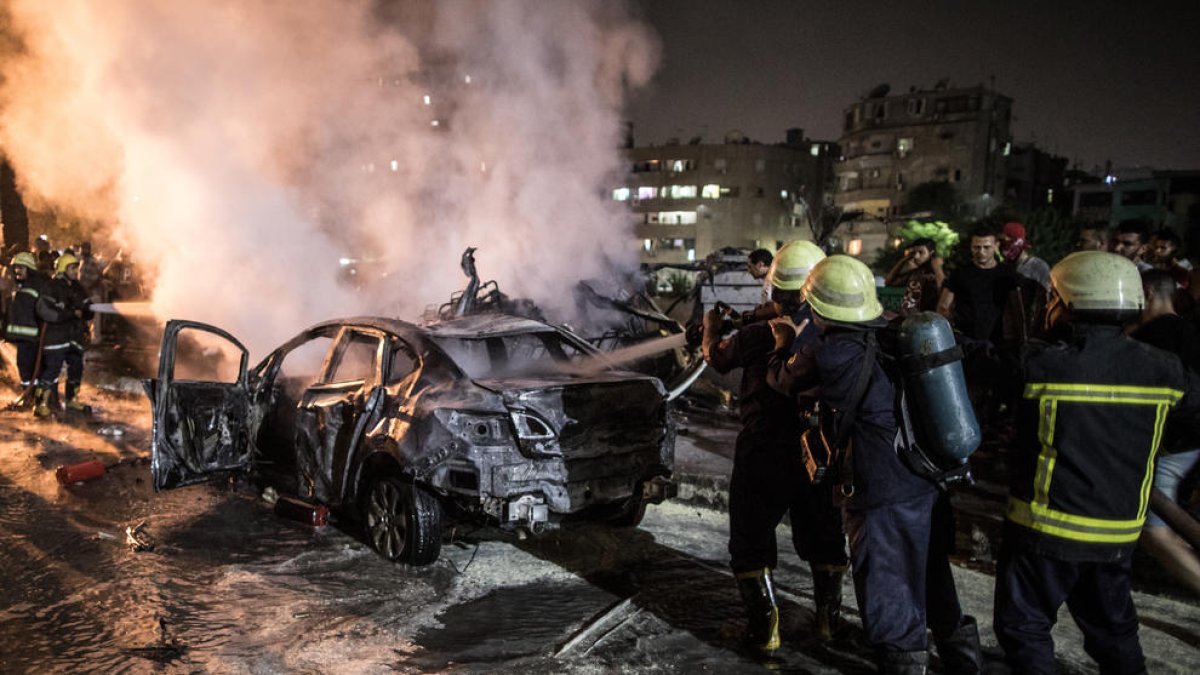 Los bomberos atajan las llamas en uno de los vehículos incendiados.