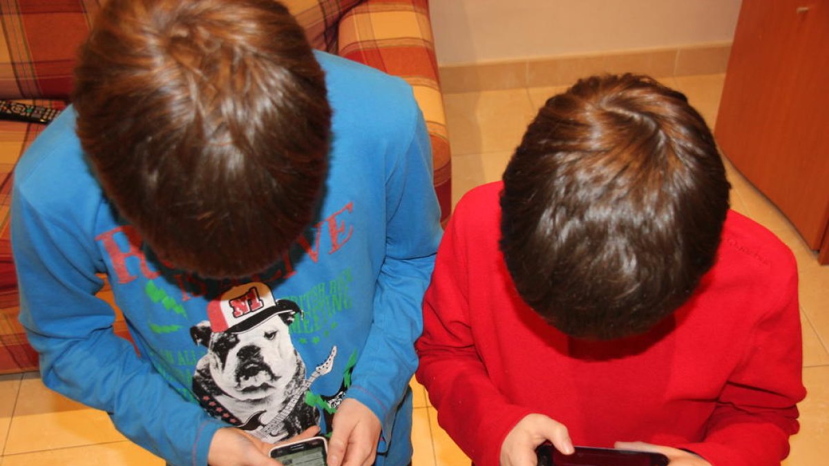 Imagen de dos niños jugando con el teléfono móvil en casa.