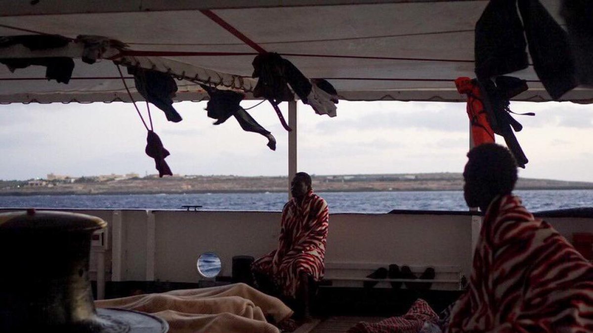 Alguns dels 147 migrants a la coberta del vaixell ‘Open Arms’ que ja es troben en aigües italianes, al davant l’illa de Lampedusa.