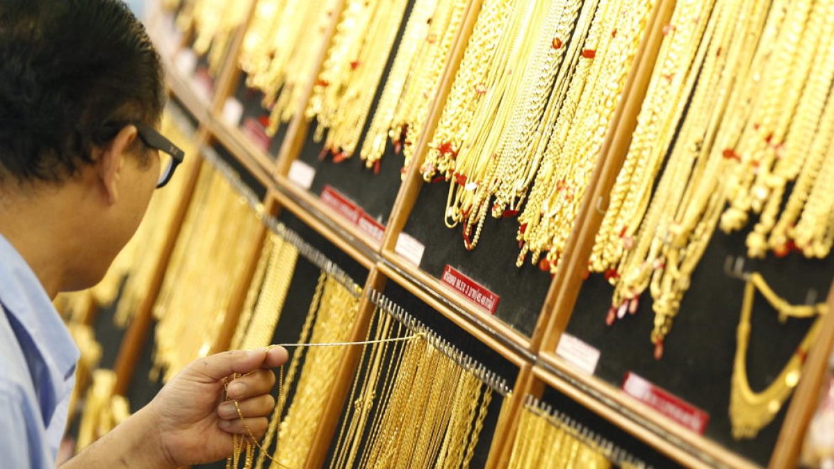 Un hombre sostiene collares de oro en un local de venta de oro.