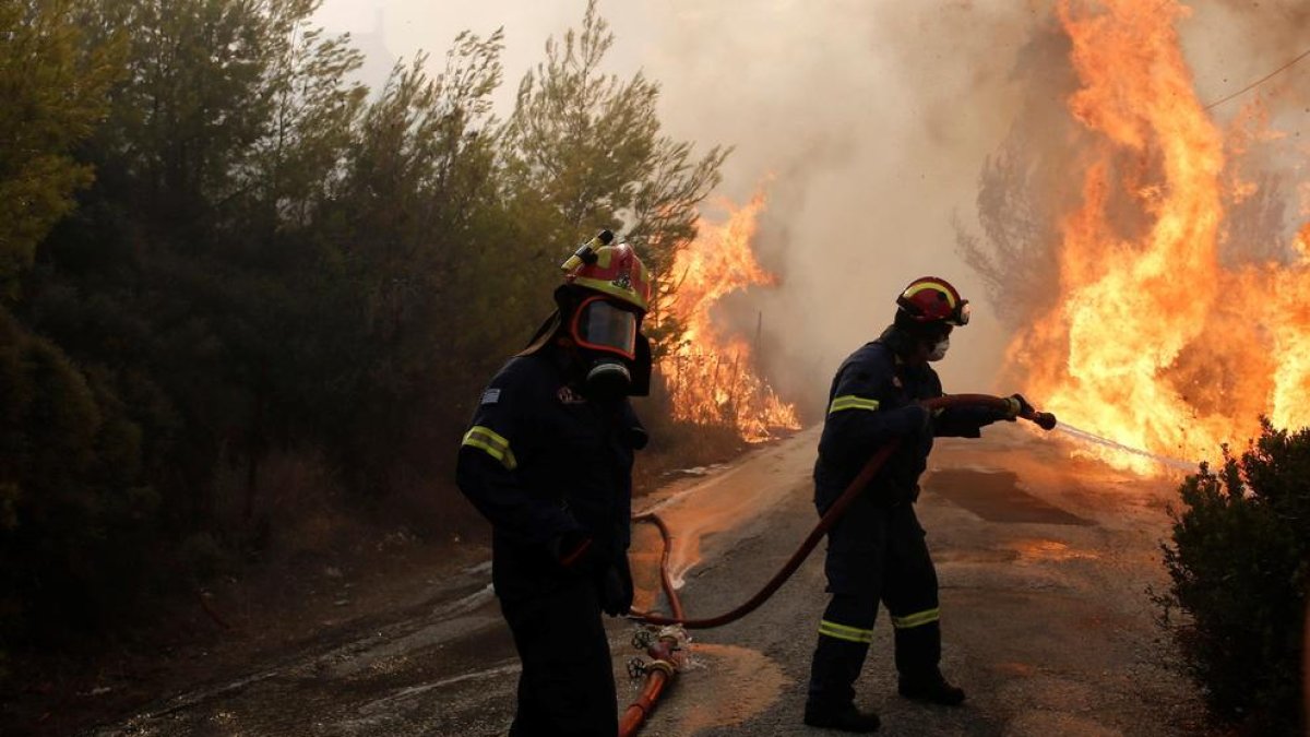 Varios bomberos tratan de extinguir un incendio en Penteli, al norte de la capital de Grecia.