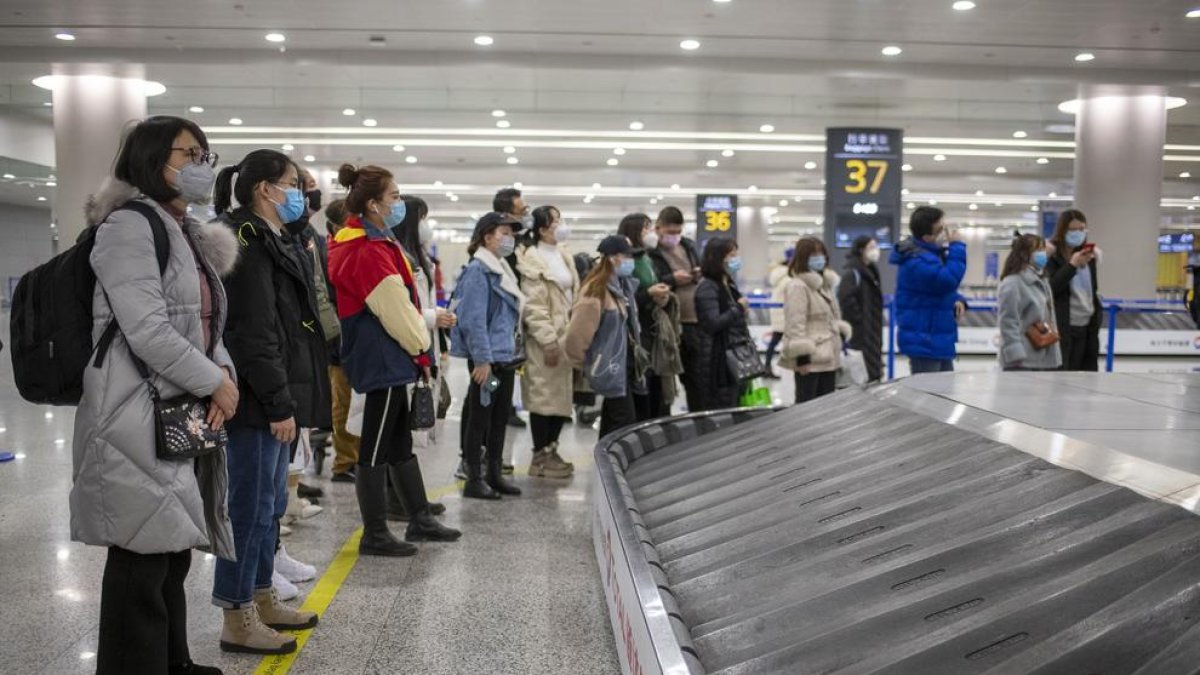 Pasajeros (con mascarilla) esperan para recoger su equipaje en el aeropuerto de Shanghái.