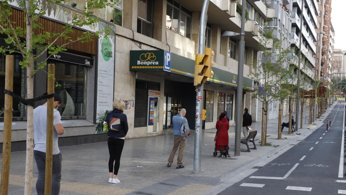 Ciutadans fan cua mantenint la distància de seguretat davant d’un supermercat al centre urbà.