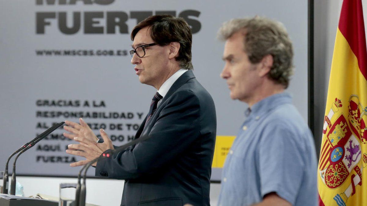 El director de CCAES, Fernando Simón, y del ministro de Sanidad, Salvador Illa, en un segundo término, en rueda de prensa.