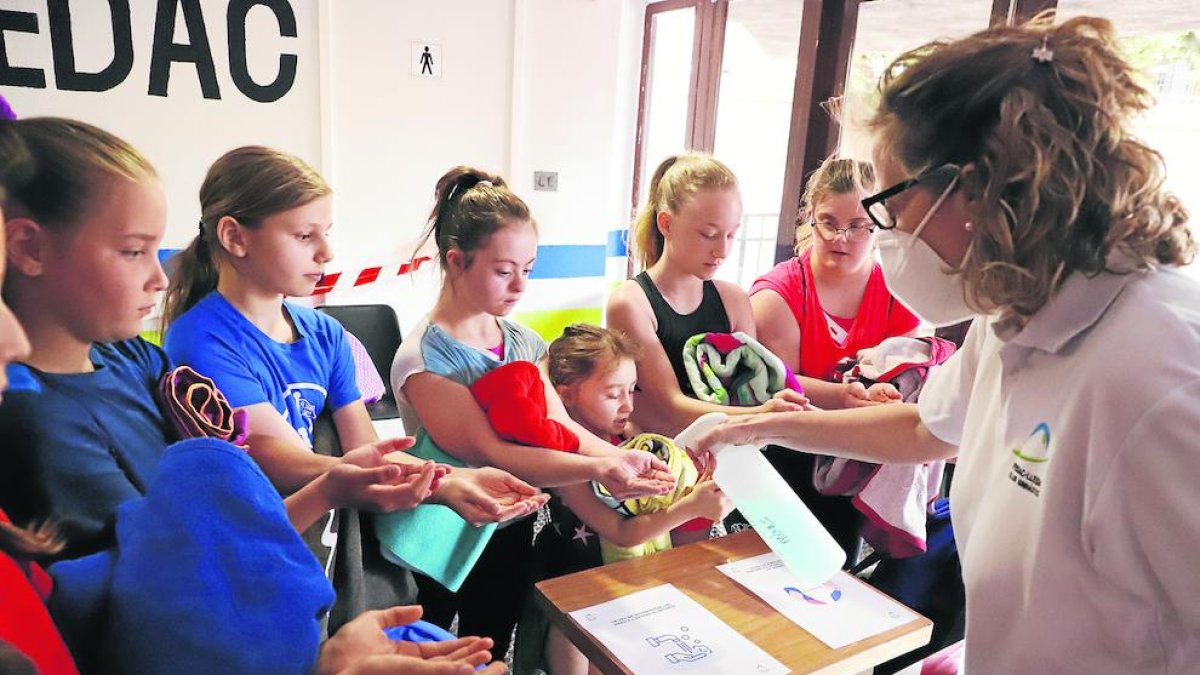 Les gimnastes segueixen un estricte protocol d’higiene abans i durant l’entrenament. A la dreta, l’entrenadora Maribel Moncasi els pren la temperatura abans d’entrar.
