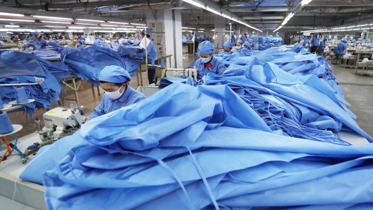 Empleados con mascarillas confeccionan camisones de aislamiento en el condado de Zouping (China).