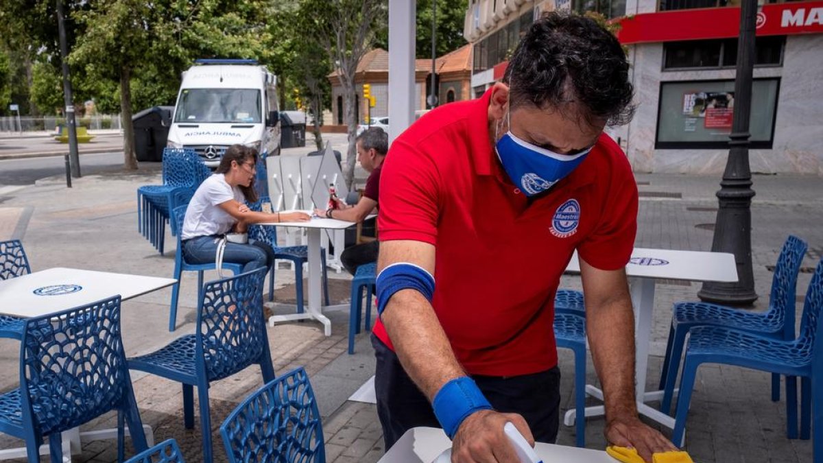 Un camarero desinfecta las mesas de la una terraza en un bar de Huelva.