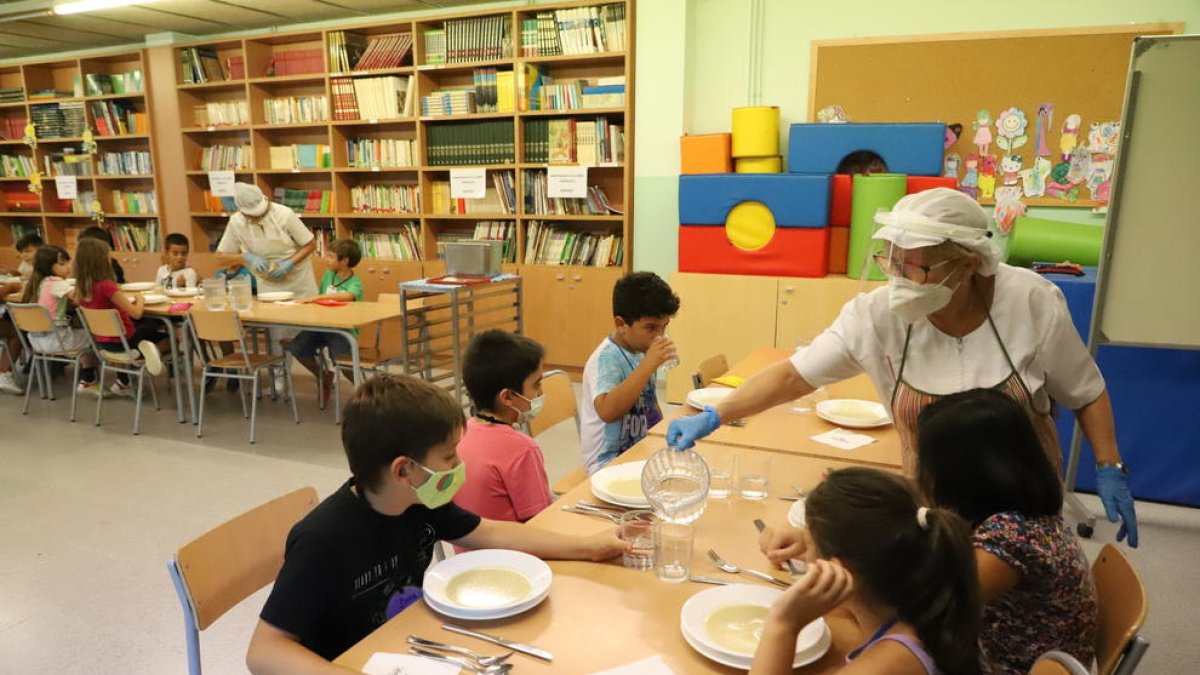Una monitora serveix aigua als alumnes del Frederic Godàs, que han de dinar a la biblioteca.