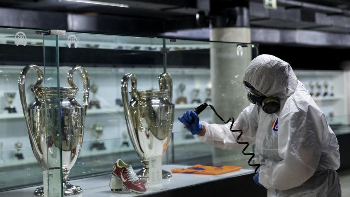 Un operario desinfecta una entantería con las Copas de Europa azulgranas.