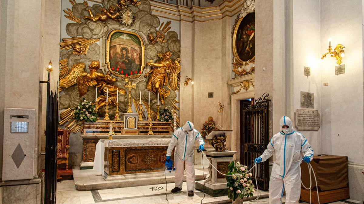 Equipos de limpieza desinfectan un altar en una iglesia en Roma.