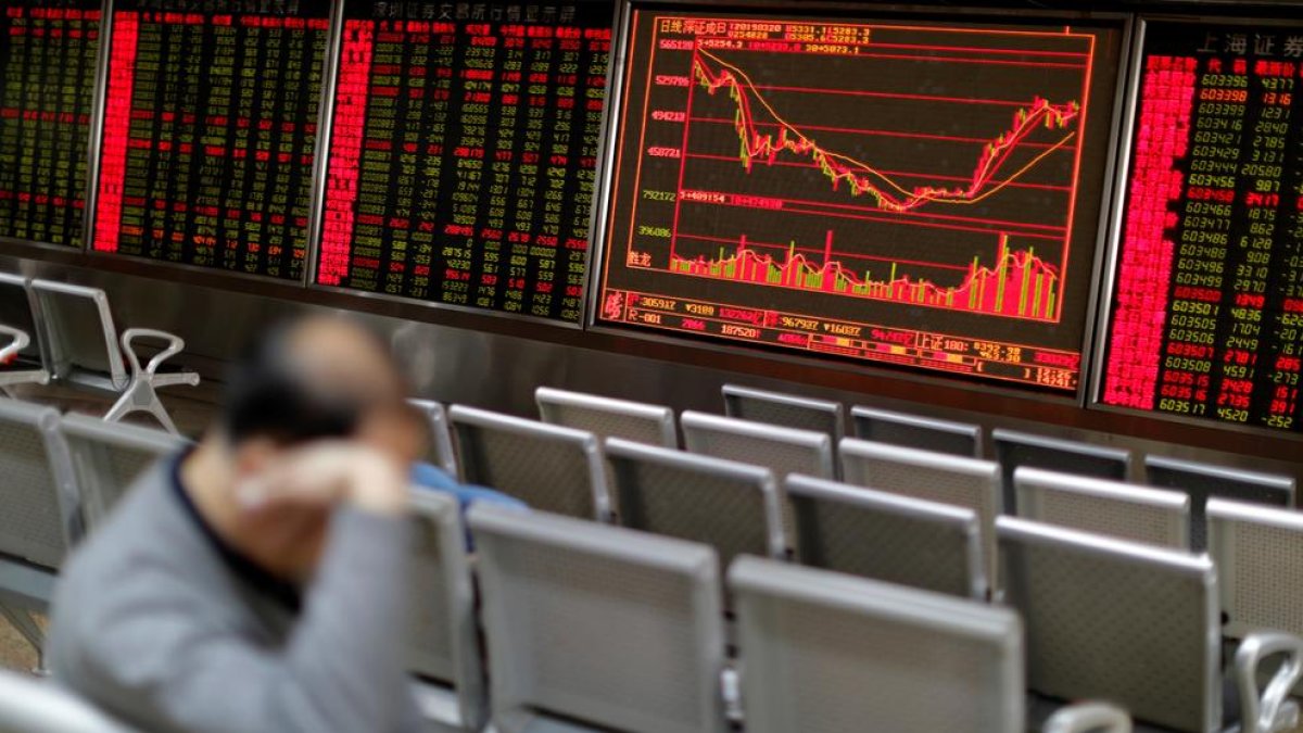 Un home descansa davant del plafó que mostra l’evolució de la borsa de Xangai, a la Xina.