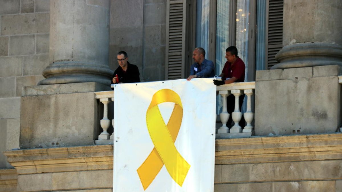 Tres operaris col·loquen de nou el llaç groc a la façana de l’ajuntament de Barcelona.