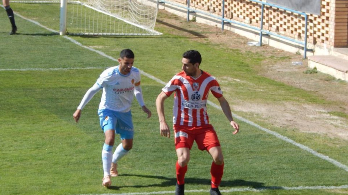Un jugador del Monzón protege el balón ante la presión defensiva de un jugador local.