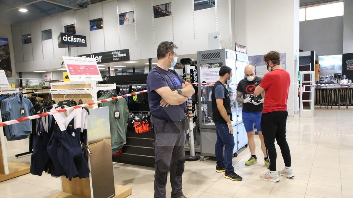 Un trabajador del Wala atiende a unos clientes junto a una zona precintada y un cartel en el suelo pidiendo distancia de dos metros.