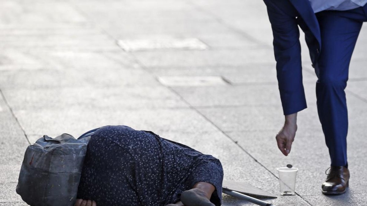 Una hombre echa una moneda a una mujer que practica la mendicidad.