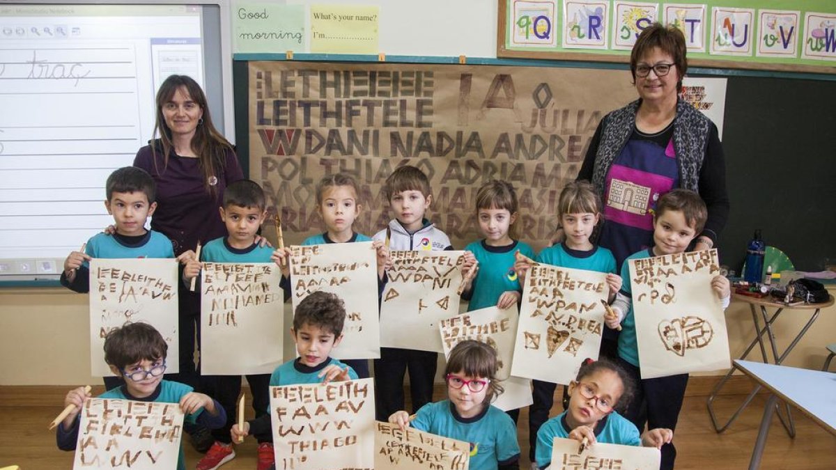 Los escolares muestran letras mayúsculas que escribieron con cañas y tinta.
