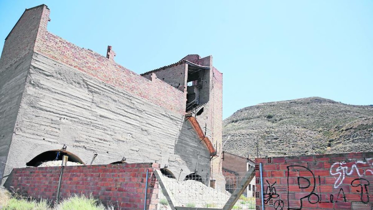 Una pared de ladrillos y una valla metálica impiden el paso hasta los edificios.