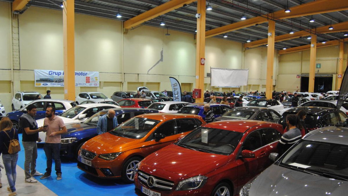 Varios visitantes, mirando coches en los pabellones feriales.
