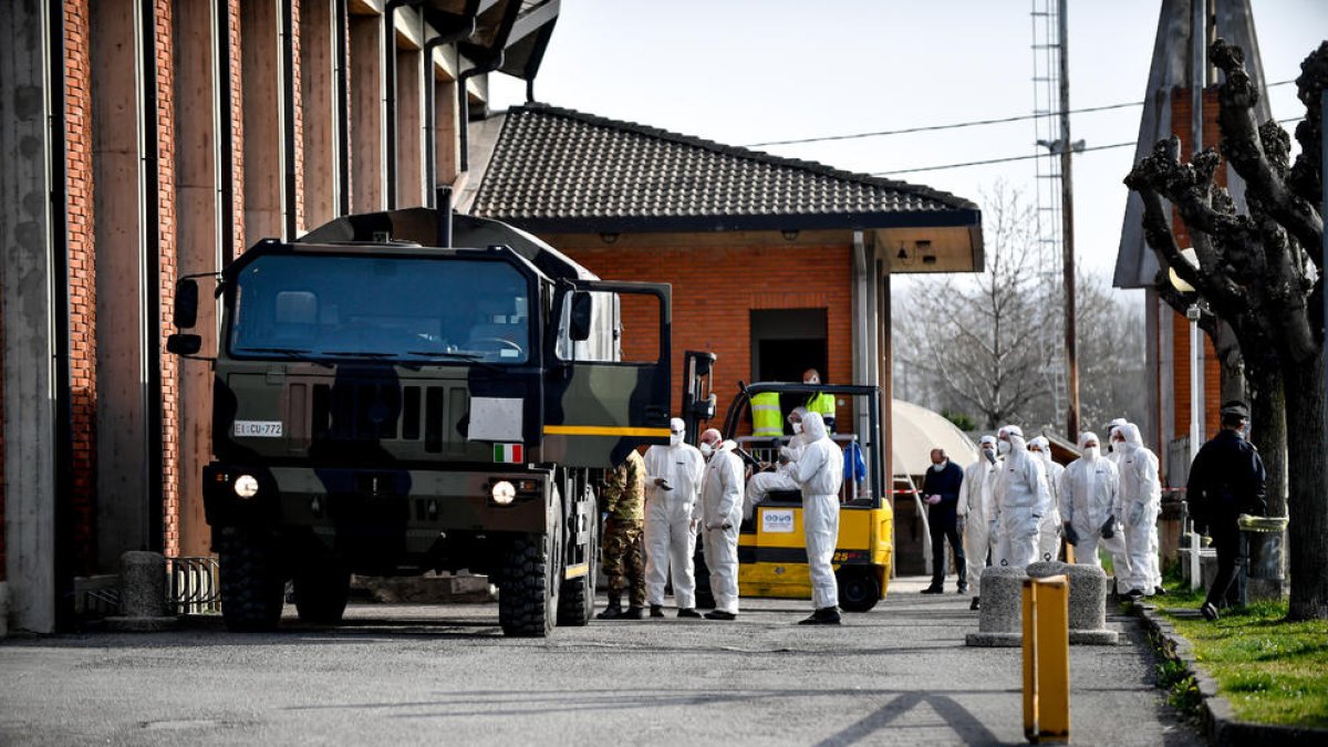 Personal mèdic de l’exèrcit italià, amb vestits de protecció, transportant taüts.