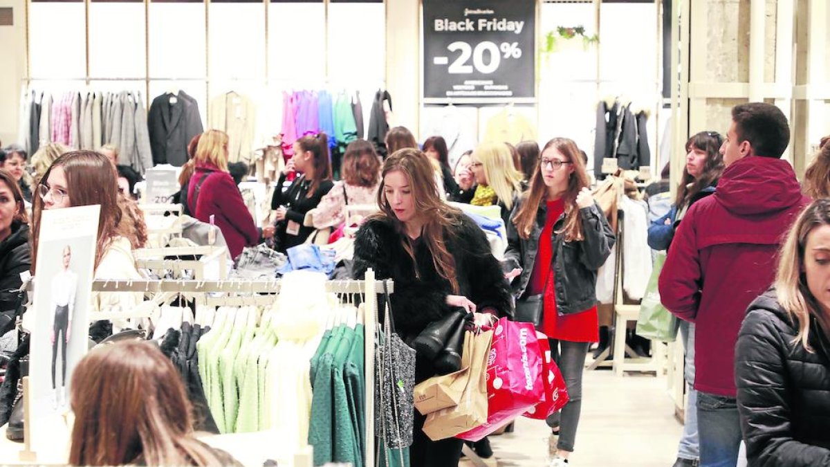 Numerosas personas en una tienda de ropa, con una joven con varias bolsas.