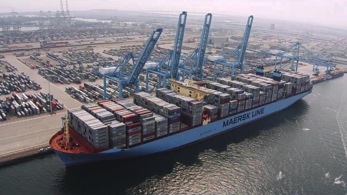 Un barco mercante carga contenedores en un puerto.