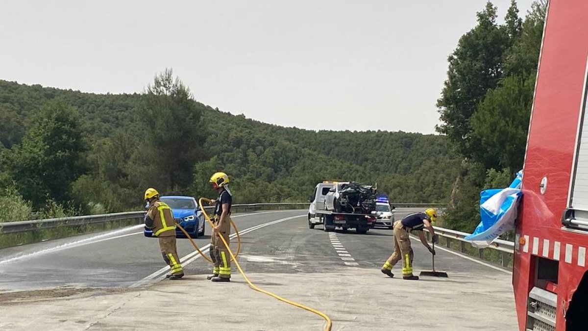 Bomberos limpiando la carretera, que estuvo unas tres horas cortada, y al fondo uno de los turismos implicados.