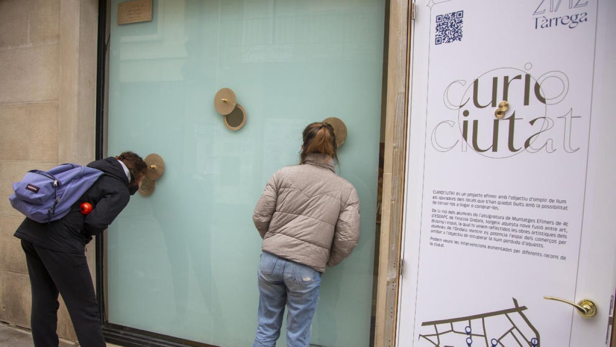 Vecinos mirando por las mirillas instaladas en uno de los escaparates de los locales vacíos de Tàrrega.