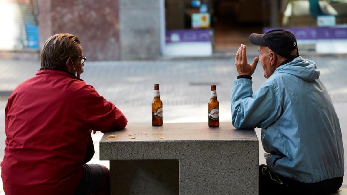 Diverses persones prenen una cervesa en un banc d'un carrer del centre de Barcelona.