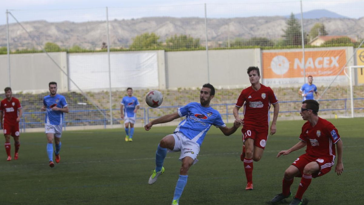 Un jugador del Binéfar controla el balón delante de dos defensas del Caspe.