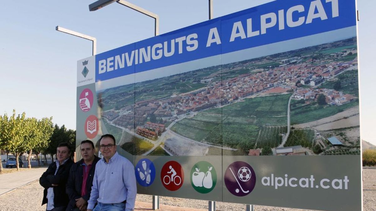L’alcalde i dos edils, amb el cartell de benvinguda al poble.