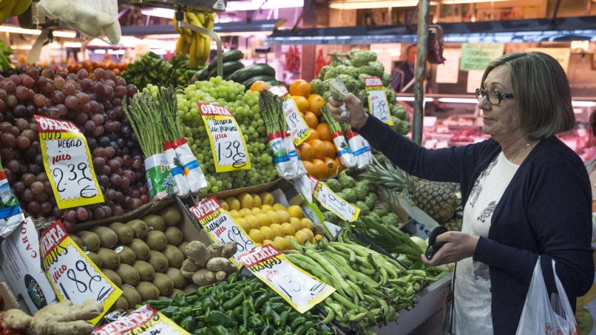 Una dona tria fruites i verdures en un supermercat.