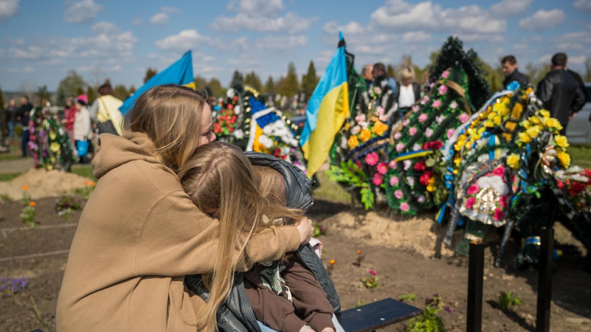 Dos mujeres ucranianas se abrazan ante la tumba de un familiar ayer en motivo del día de los muertos.