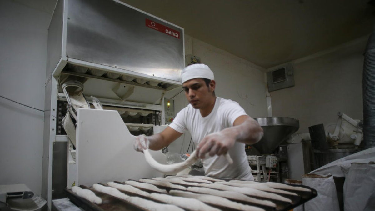Un trabajador prepara barras de pan en el obrador.