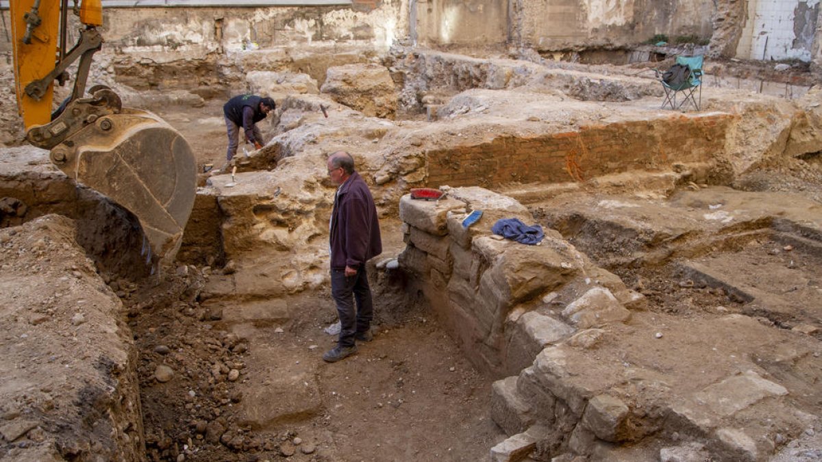 Los restos de la muralla, en el suelo junto a la excavadora y a la derecha, restos de un arco