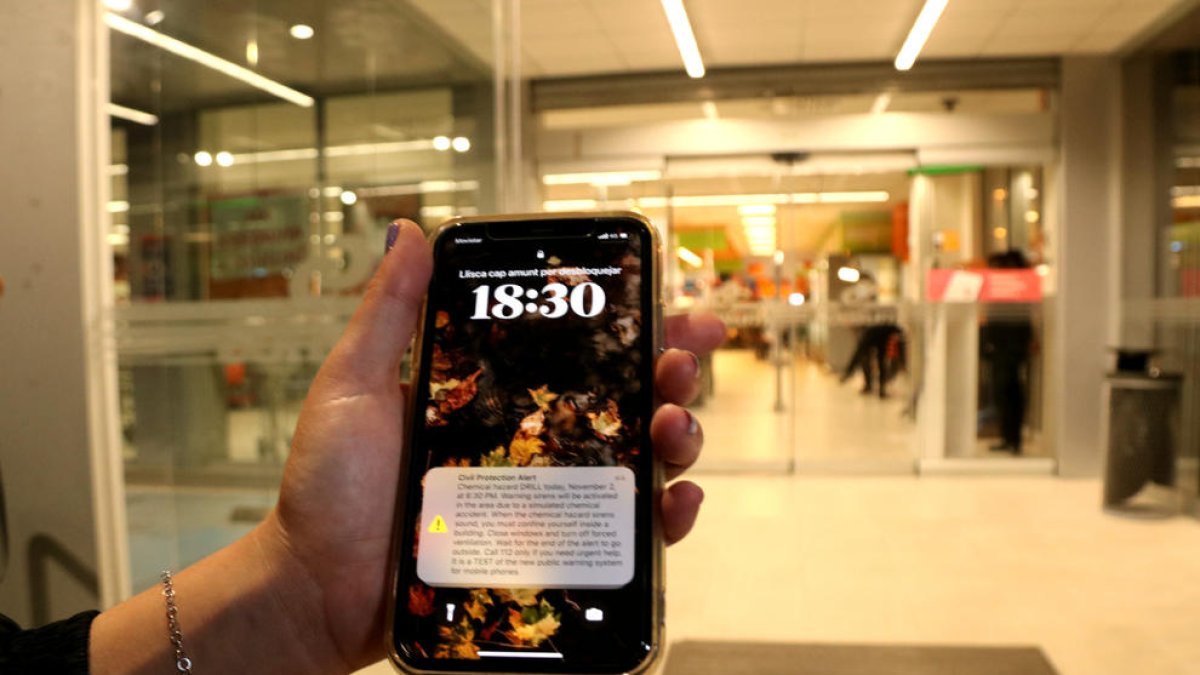 Una vecina muestra el mensaje recibido al teléfono móvil para iniciar el simulacro en las puertas de un supermercado de la Canonja
