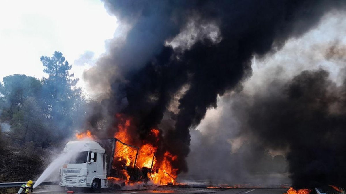El camió incendiat aquest divendres a l'AP-7 i els Bombers treballant-hi.