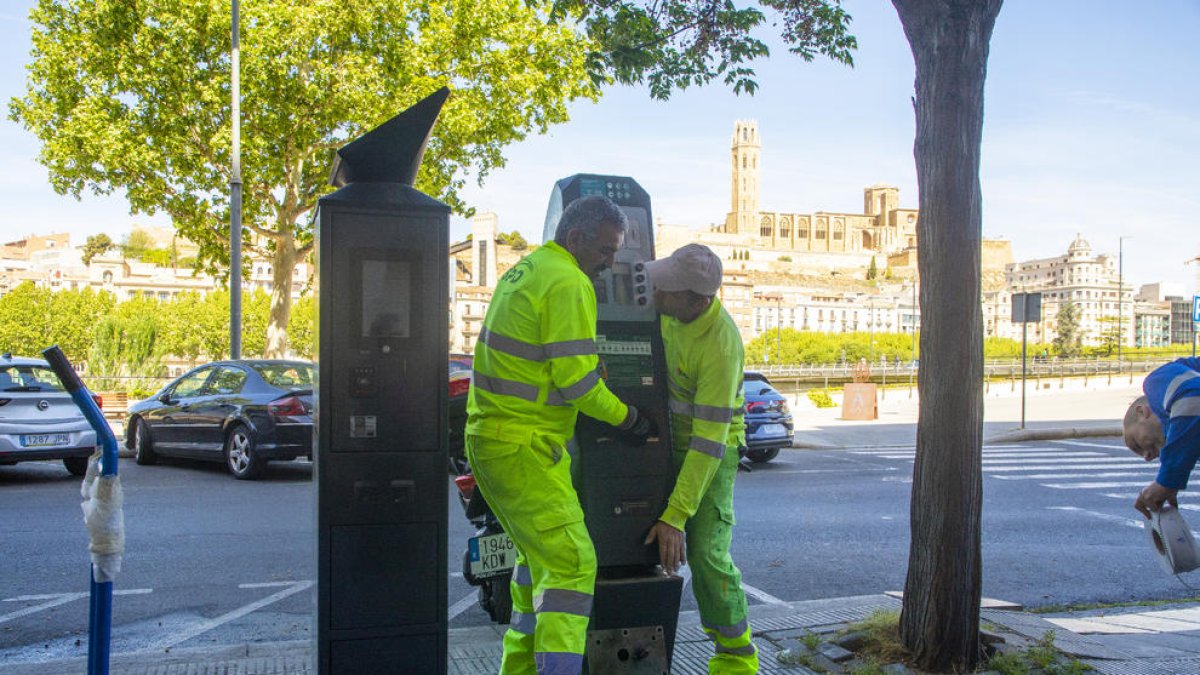Dos operarios municipales retiran un parquímetro de Eysa, que está al lado de uno nuevo de la EMAU.