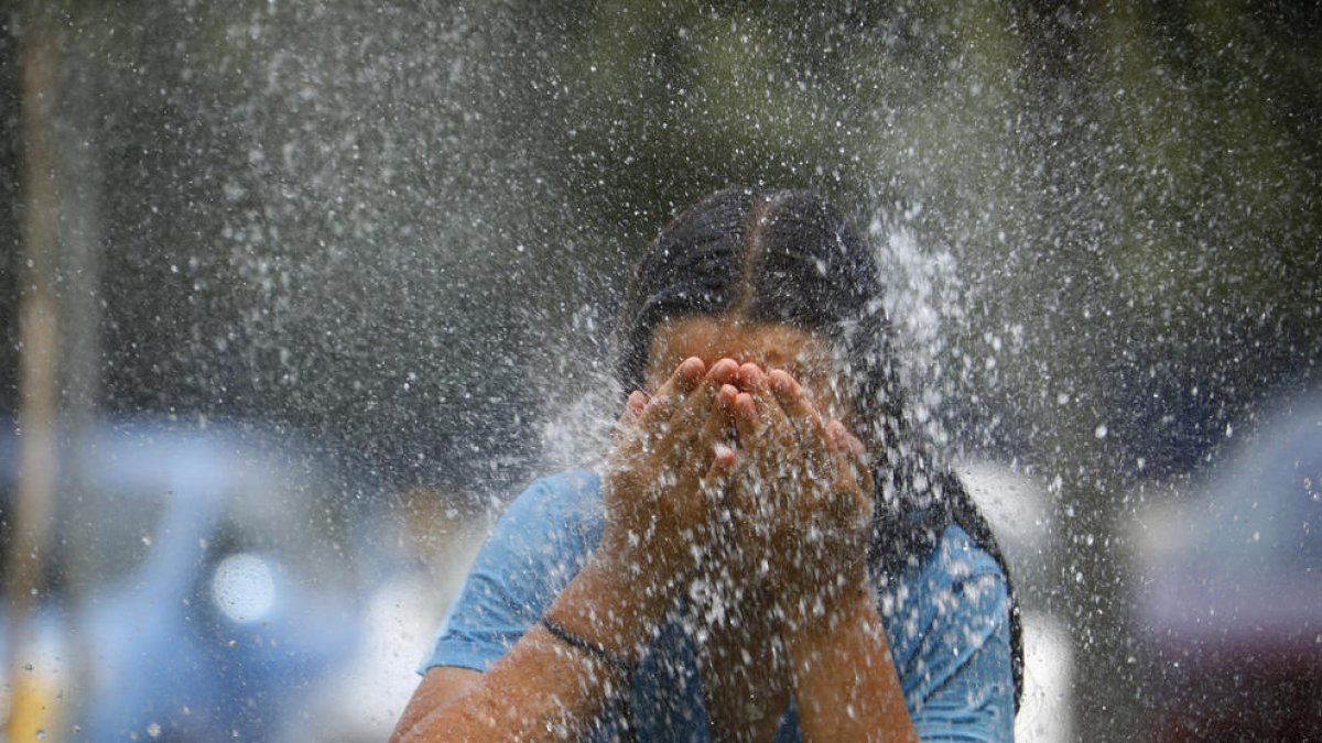 Una joven se refresca en una fuente.