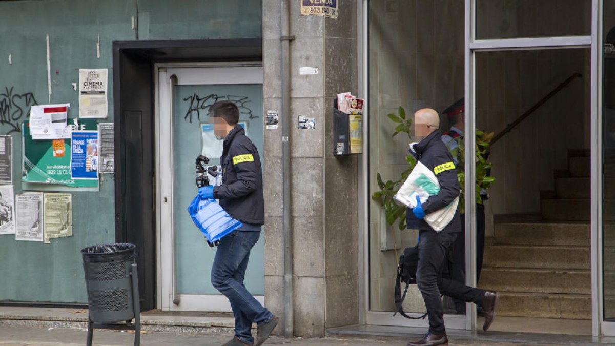 Dos agentes de los Mossos saliendo del número 80 de la avenida Alcalde Porqueres, donde fue hallado el cadáver.