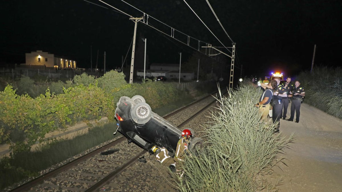 El coche volcado sobre la vía del tren y los servicios de emergencias que se desplazaron hasta el lugar.