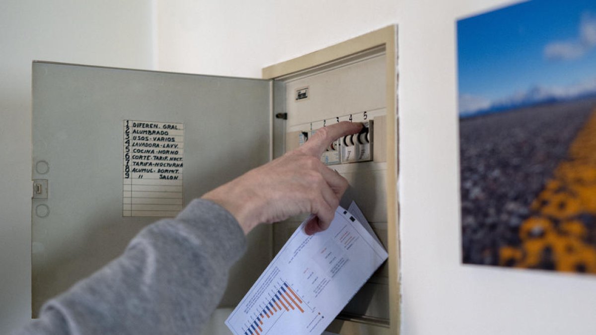 Un usuario sube los plomos de la luz con una factura de luz en la mano.