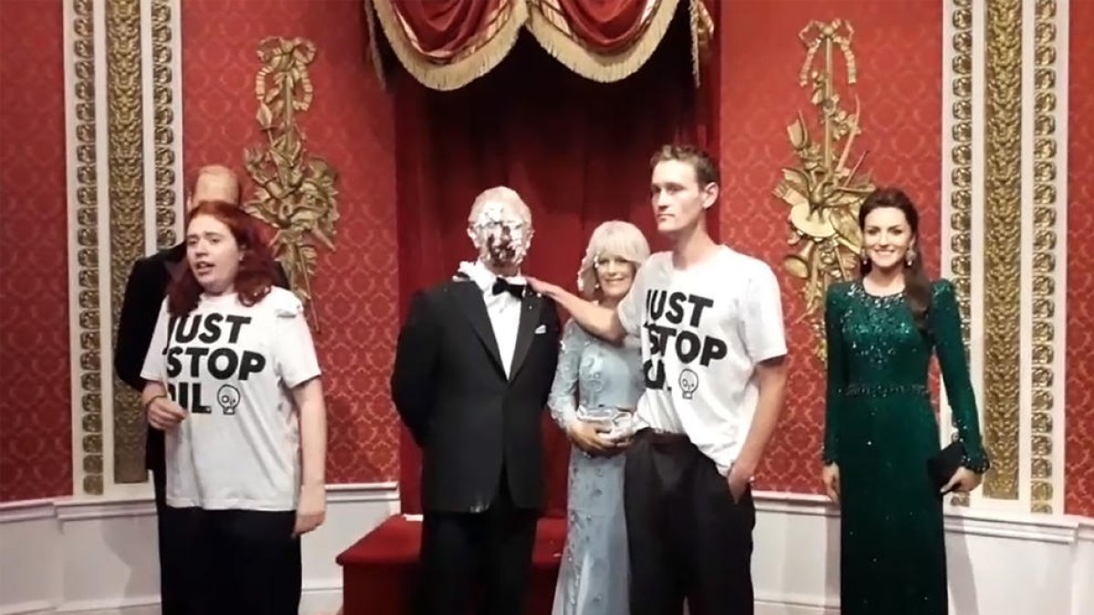 Els dos activistes, amb la figura de Carles III amb el pastís estampat i la resta de figures de la casa reial.