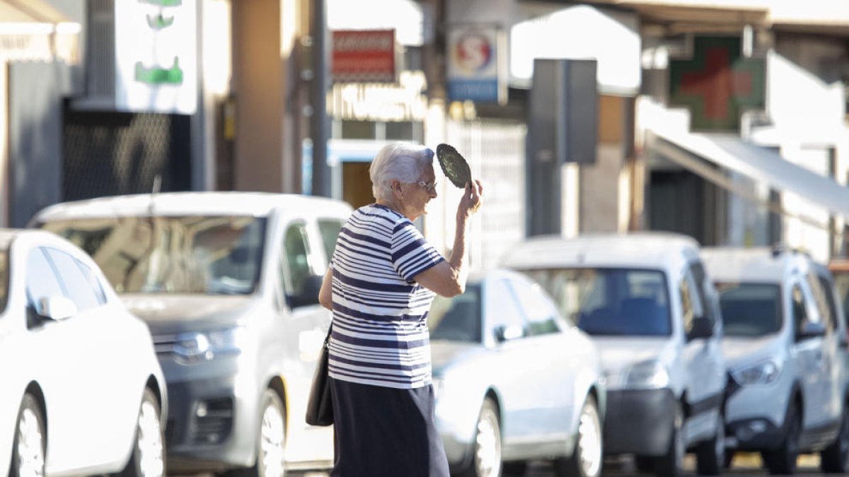 Una mujer se protege del sol mientras cruza la calle en Lleida.
