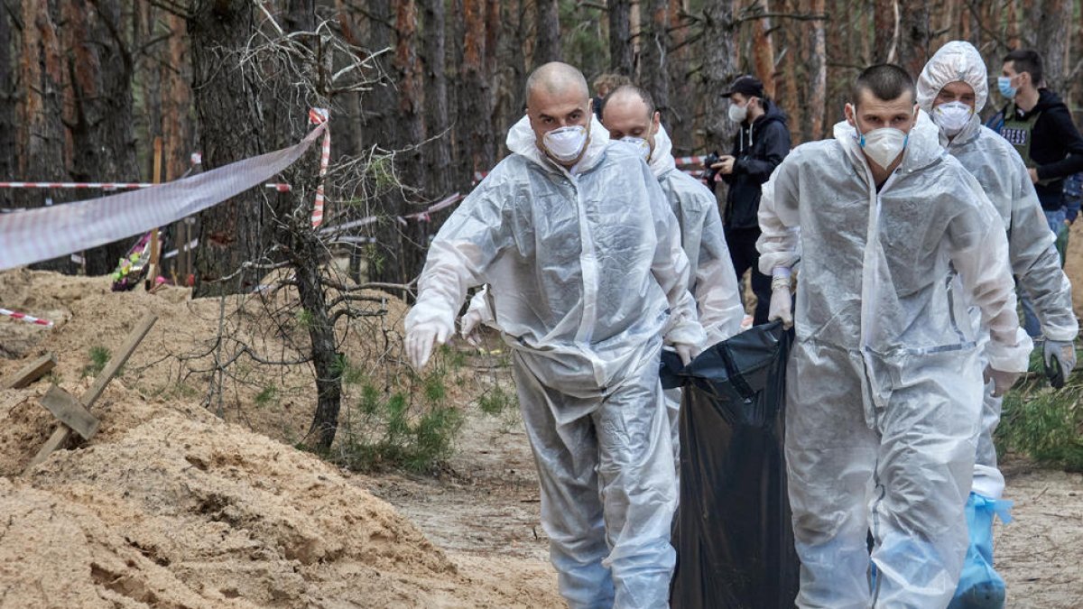 Trabajadores ucranianos transportan cuerpos de tumbas halladas en septiembre en Izyum, en Járkov.