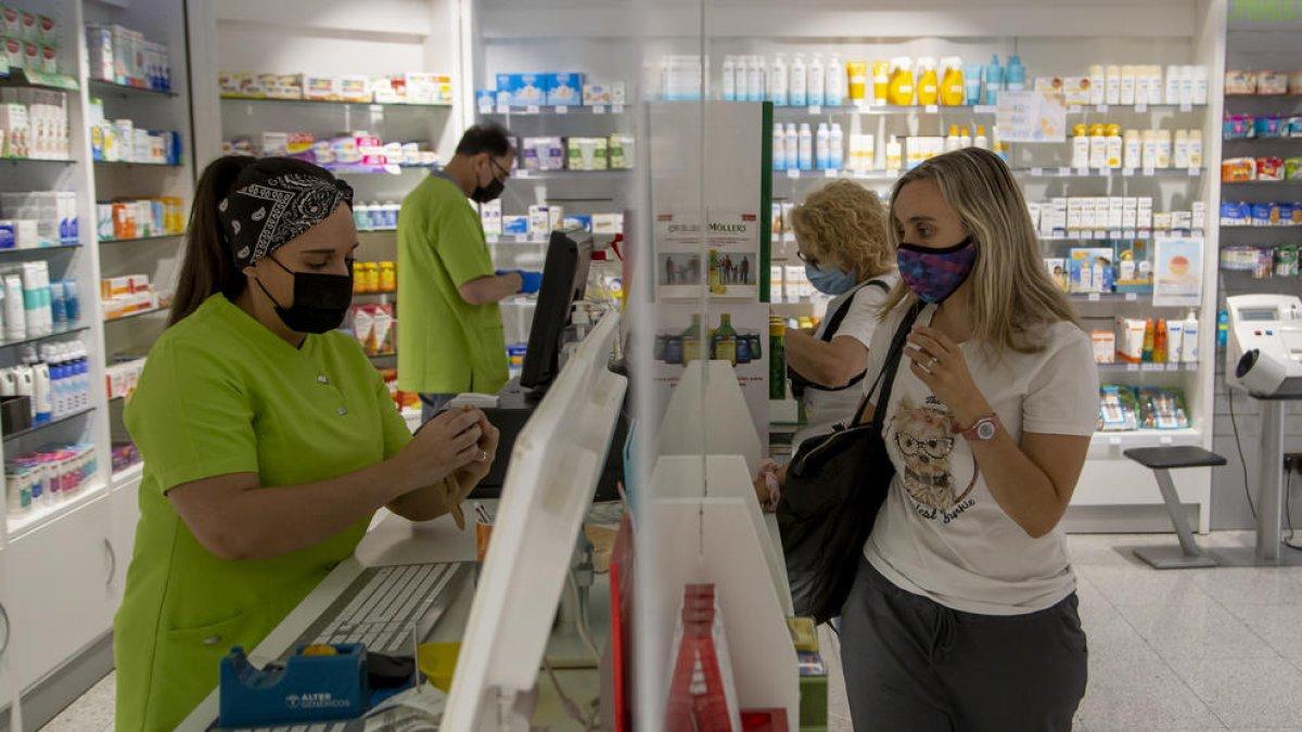Treballadors i clients d’una farmàcia amb mascareta, que deixarà de ser obligatòria en aquests espais.