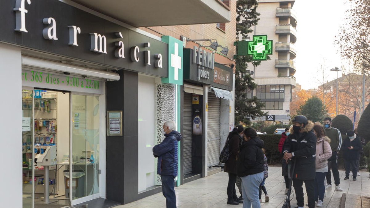 Imatge d’arxiu de diverses persones esperant per entrar en una farmàcia.