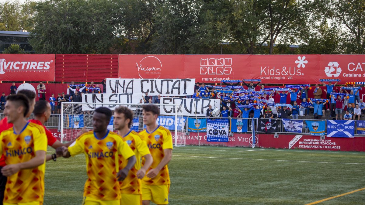 Jugadores del Lleida, el domingo en Vic con la pancarta al fondo que mostró la afición leridana. - JORDI ECHEVARRIA