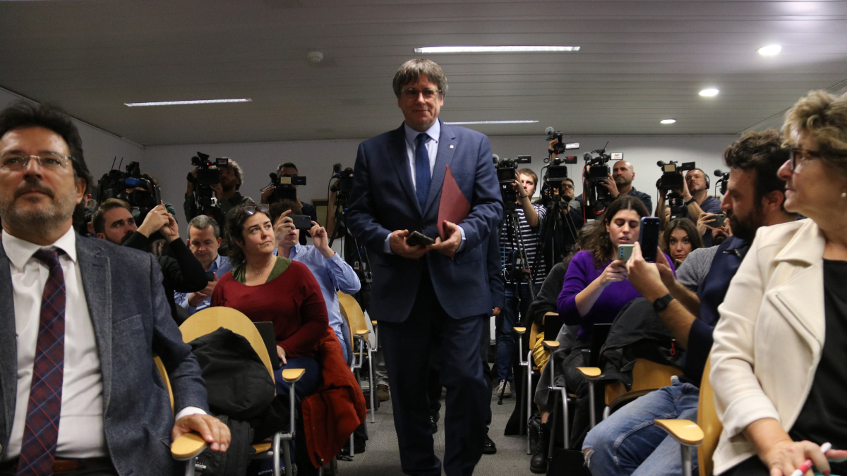 Puigdemont es dirigeix a explicar l’acord davant dels líders del seu partit, com Isidre Gavín. A la dreta, Cerdán entra a la sala on l’esperen els periodistes. - ACN