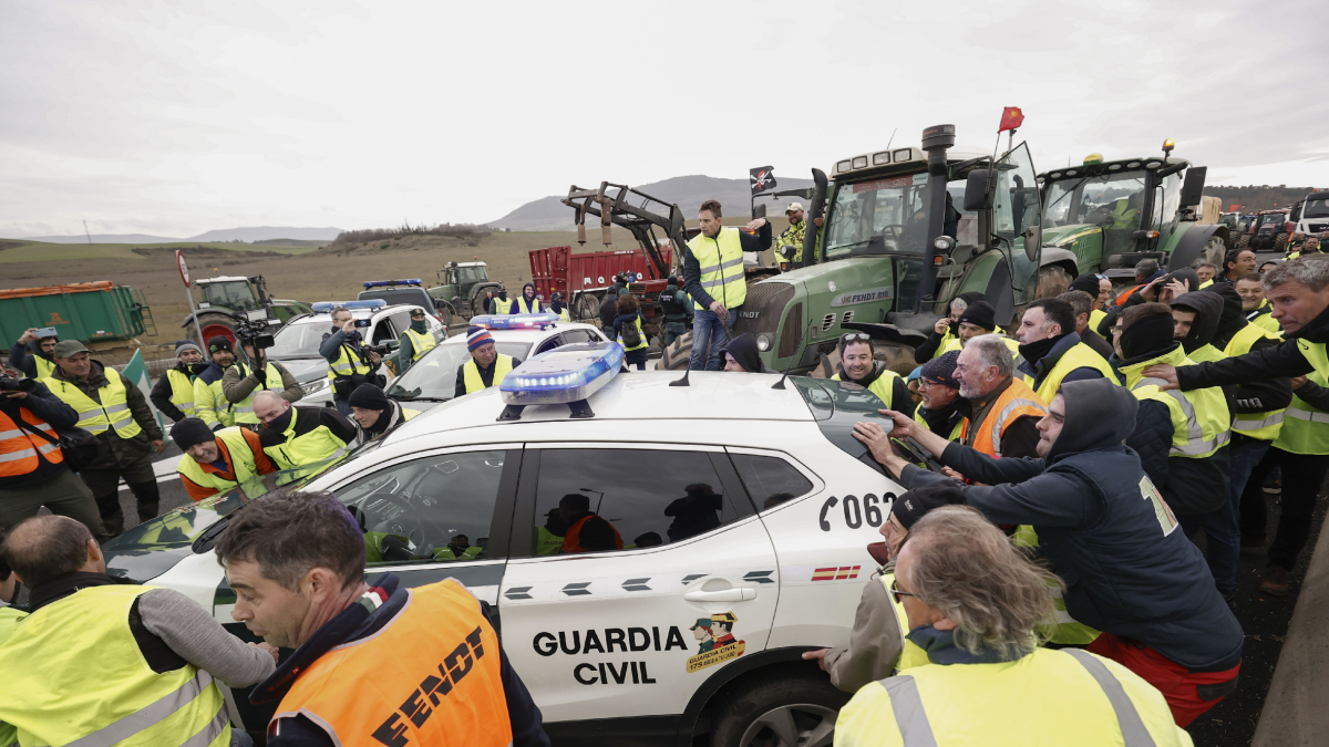 Un grupo de agricultores empuja un coche de la Guardia Civil que les impedía entrar con los tractores en una carretera de Navarra. - EFE